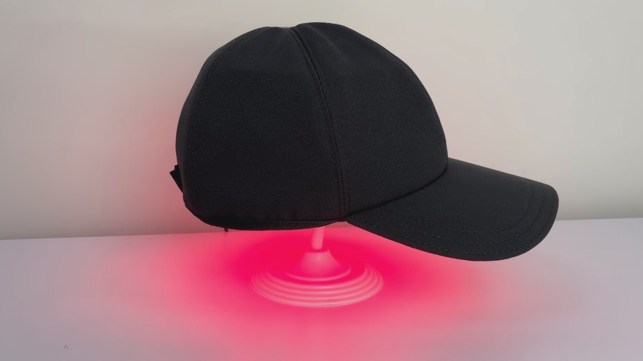 Black brimmed LED cap on a display stand with red light visible beneath the crown